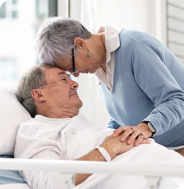 Elderly man in a hospital bed with their partner embracing them